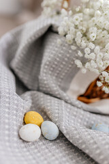 A wicker brown basket, inside which, on a gray linen napkin, are painted yellow, blue, white eggs and white small flowers.  Spring background for Easter. Mock up. Space for text
