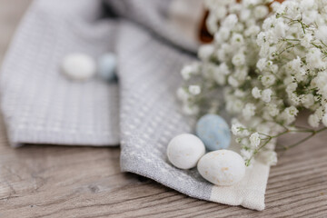 A wicker brown basket, inside which, on a gray linen napkin, are painted yellow, blue, white eggs and white small flowers.  Spring background for Easter. Mock up. Space for text