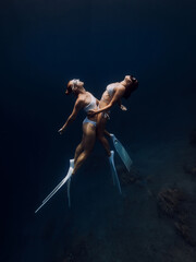 Fototapeta na wymiar Freedivers girls hugging and glides in ocean. Freediving with woman couple in underwater