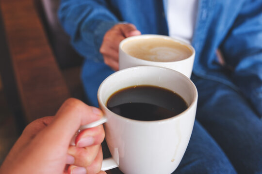 Closeup image of a couple people clinking white coffee mugs in cafe