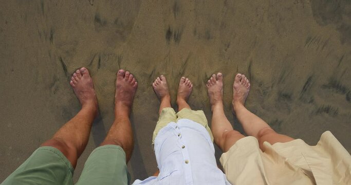 Man's, woman's and child's feet on sand are washed by sea waters. Tanned feet of people in sea foam. The first day of the long-awaited vacation, which a happy family of three spends on the beach.
