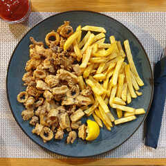 Fried calamari squid rings served with fries on grey plate  with tomato sauce on table with woven placemat