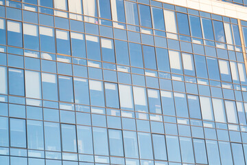 Fototapeta na wymiar Modern office building facade. Tall business center with a glass facade. Construction of a glass facade structure. The glare of the sun on the glass wall of a skyscraper