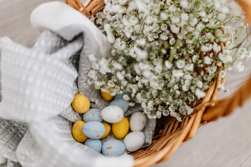 Blue, yellow, white eggs and white small flowers lie in a basket close-up. Spring Background for Easter