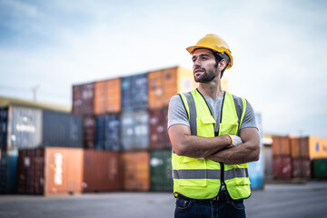 Caucasian warehouse worker in uniform with hard hat standing in container port terminal. Area...