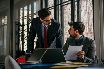 Two businessmen cooperate while going through reports in the office.