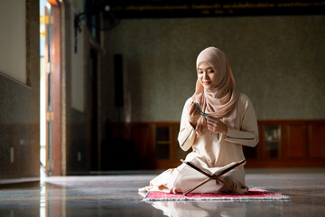 The image of an Asian Muslim woman in the Islamic religion in hijab in cream color. Sitting reading the Quran and having a happy smiling face Staying in a beautiful mosque out of respect for God.