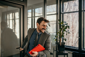 An attractive Caucasian businessman in a suit opens an office door, holding a tablet and entering his office.