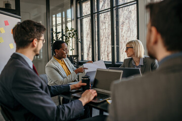 Smiling diverse female entrepreneurs talking to their colleagues about business reports of the economy grow at a meeting in the office.