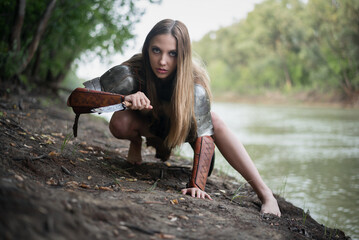 Beautiful girl warrior with the knife is hunting on the river shore.