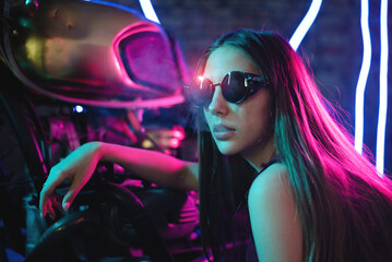 Plakat Girl a motorbiker near the cyberpunk motorcycle in the neon lights.