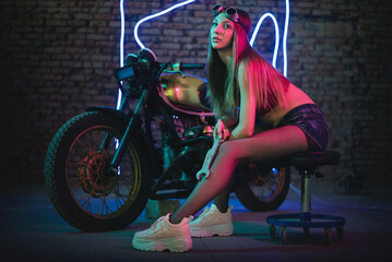 Plakat Girl a motorbiker near the cyberpunk motorcycle in the neon lights.