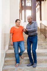 Senior man helping his wife to go down the stairs