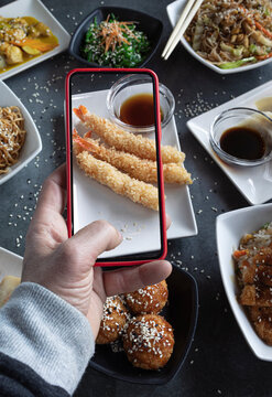 The man takes a photo on his smartphone Dishes with rice, noodles, gyozas, chicken wakame. food blog. Vertical image for social sharing