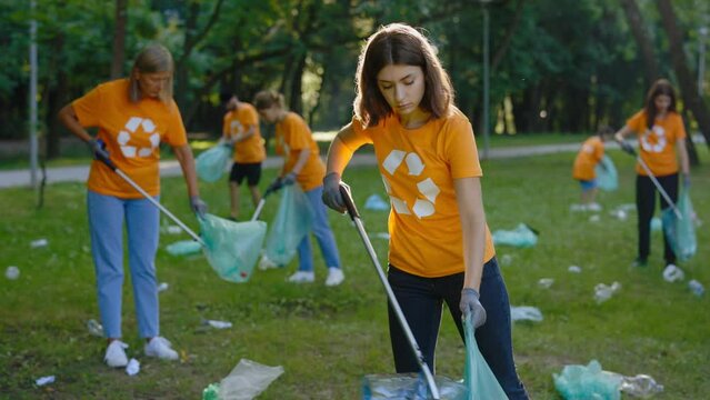 Woman Eco Volunteer Using Trash Picker While Collecting Garbage in Bin Bag. Group of Eco Activists in T-Shirts with Recycling Symbol Cleaning Park. Concept of Ecology, Recycling