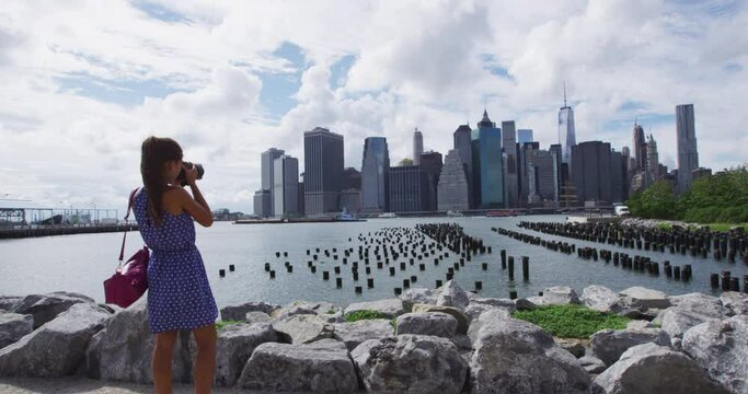 New York tourist woman taking picture with camera of Manhattan city skyline waterfront lifestyle. People walking enjoying view of downtown from the Brooklyn bridge park Pier 1 salt marsh