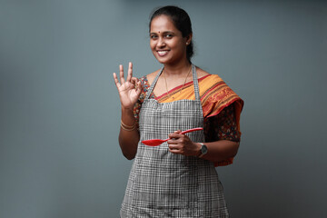Indian ethic woman wearing apron and holding spatula showing a like gesture