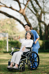 Elderly asian senior woman on wheelchair with Asian careful caregiver and encourage patient, walking in garden. with care from a caregiver and senior health insurance...