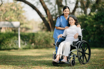 Elderly asian senior woman on wheelchair with Asian careful caregiver and encourage patient, walking in garden. with care from a caregiver and senior health insurance...
