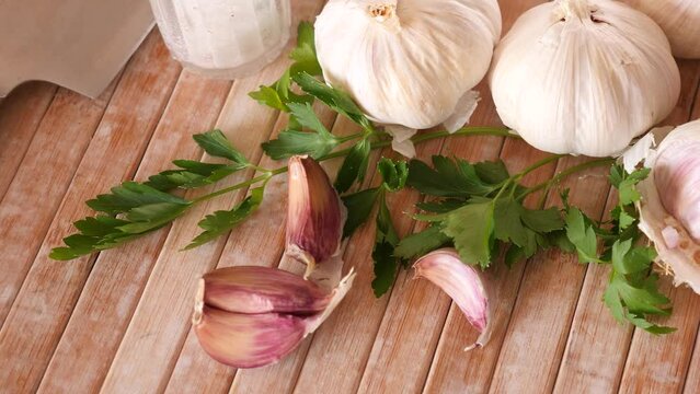 Cutting board with fresh seasonings on a wooden background. White garlic heads and cloves and parsley leaves. Condiments