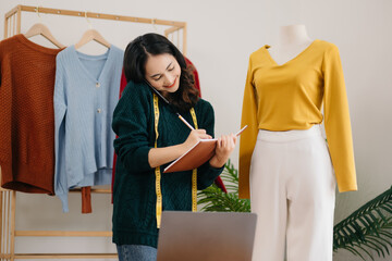Fashion designer woman talking smart phone and using laptop with digital tablet computer in modern studio in morning light