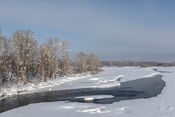 winter river with thaw and forest on the bank
