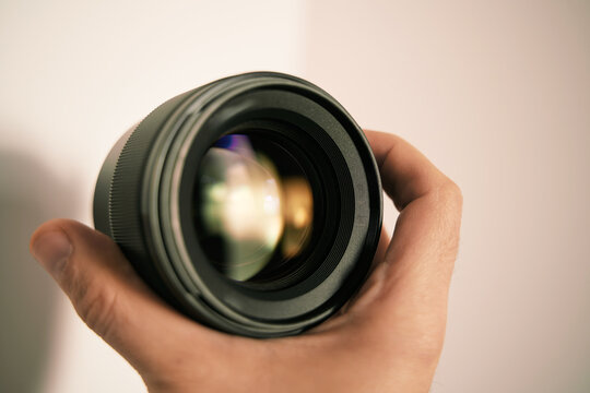 Modern digital camera lens in hand close up over light background. Banner image with a copy space of a lens in hand.