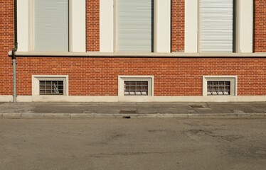 Basement windows on brick wall facade with tarmac sidewalk and urban road in front. Background for copy space.