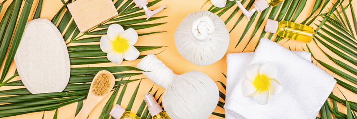 Spa massage Aromatherapy body care background. Spa herbal balls, cosmetics, towel and tropical leaves on orange table. Top view, flat lay, overhead, copy space. Beauty and health care concept