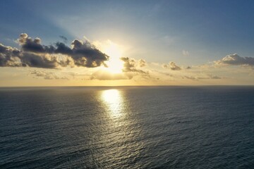 Shot of a golden burning sun in the cloudy sky about to set on the horizon of the sea.