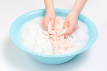 Female hands washing pink towels in basin on white background.
