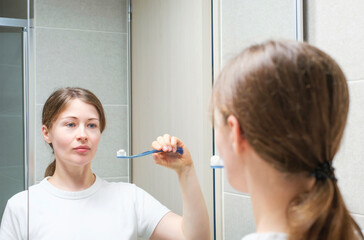 Young woman brushing teeth standing in front of mirror, oral care concept.