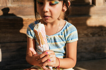 Close up of a Little girl eating an ice cream sitting in the street