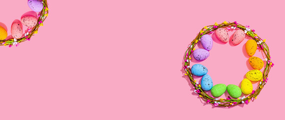 Obraz na płótnie Canvas Easter wreath with colorful eggs on pink background. Artificial floral decor, festive symbols