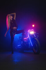 Fototapeta na wymiar Young beautiful girl in the neon lights stands near the motorbike.