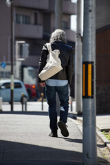 昼の街の道で歩く無職のシニア男性の後ろ姿