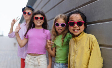 Happy friends posing together in city, standing in front of concrete wall and looking at camera.