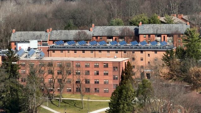 Solar panels on top of college dorms. Long aerial zoom shot of brick buildings with photovoltaic array on roof. Sustainable energy in winter theme.