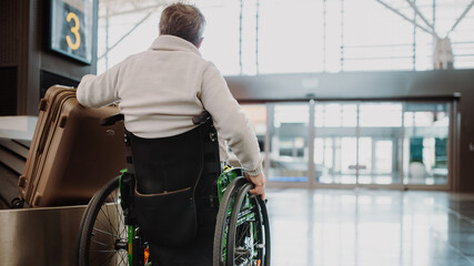 Rear view of man on wheelchair at airport with his luggage.