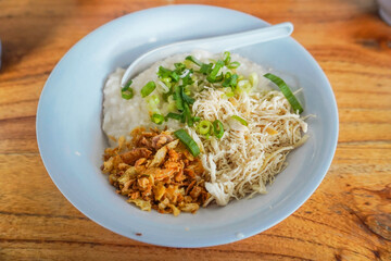 Indonesian Chicken Porridge, Indonesian Traditional Food Consist of porridge mixed with chicken meat served with egg, vegetables, and crackers on blue plate isolated on white background