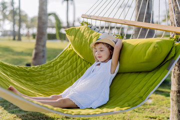 Little girl in straw hat lying in hammock and enjoying summer exotic vacation.