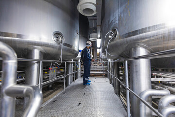 Male work inspection process stainless steel tanks and pipe with pressure meter in equipment tank facility for milk cellar at the with vertical stainless mixing tank