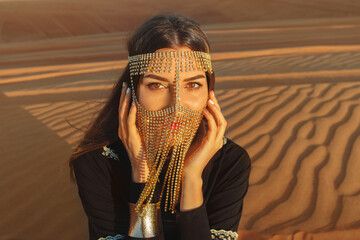 Beautiful woman in brilliant Burqa mask among the Dubai desert at sunset time.Arabian style