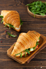 Breakfast croissants sandwiches with salmon, cream cheese and arugula on a wooden table.