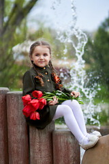 Portrait of a cute little girl in uniform with flowers on the background of a waterfall. Victory Day, May 9 holiday.