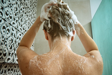 Back view of naked woman taking shower in shower stall. Woman washing her hairs in bathroom....