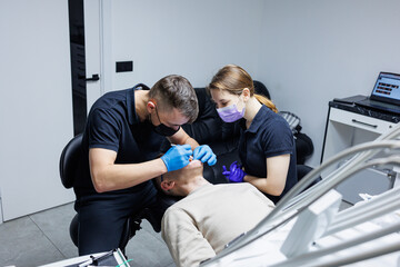 An orthodontist with an assistant treats teeth using dental instruments. Dental office. Orthodontic treatment of teeth