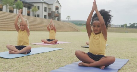 Video of focused diverse girls practicing yoga on mats in front of school