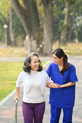 Image of caring female caregiver talking, supporting, helping elderly woman while walking in outdoor