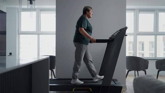 Home Fitness Workout Of Aged Woman, Senior Lady Walking On Treadmill In Modern Apartment